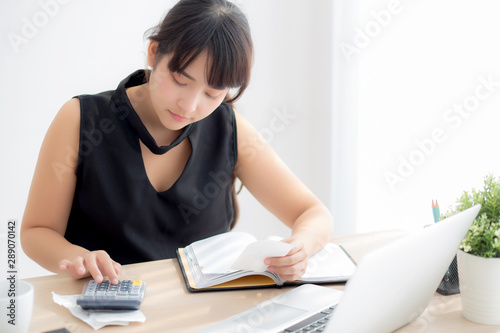 Beautiful young asian woman calculating expenses household and writing notebook on desk, girl checking bill and stress and note, female worry debt and tax, finance and business concept.