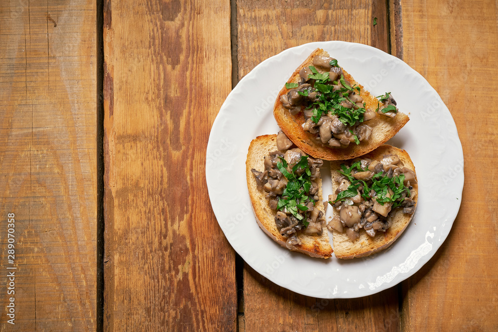Toasts with mushrooms on white plate on wooden kitchen table