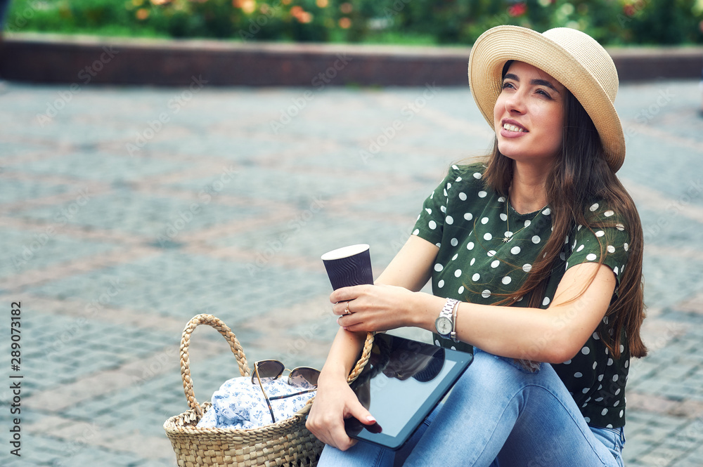Portrait of a young girl in casual clothes in the city . A woman in a wide-brimmed hat holding a Cup of coffee