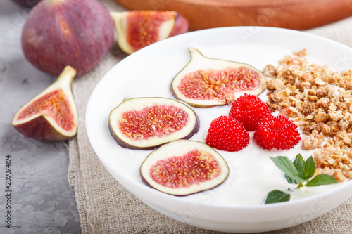 Yoghurt with raspberry, granola and figs in white plate on a gray concrete background and linen textile. side view, selective focus.