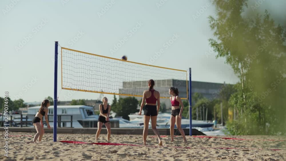 Group of four young female athletes playing beach volleyball. Barefoot