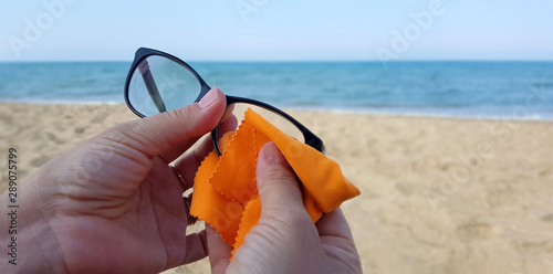 Donna che pulisce occhiali da vista sulla spiaggia photo