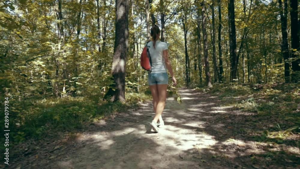 The young woman millennial in jeans shorts with a backpack walking on road in the forest summer. Active healthy lifestyle on outdoor. Man in solitude with nature. The young woman millennial in jeans shorts with a backpack walking on road in the forest summer. Active healthy lifestyle on outdoor. Man in solitude with nature.