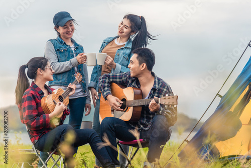 Group of Asian friends having fun eating barbecue outdoor while camping and play guitar.