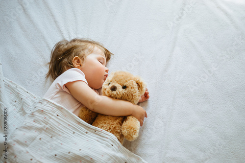 Little baby sleeping on bed at home with soft toy. Free space