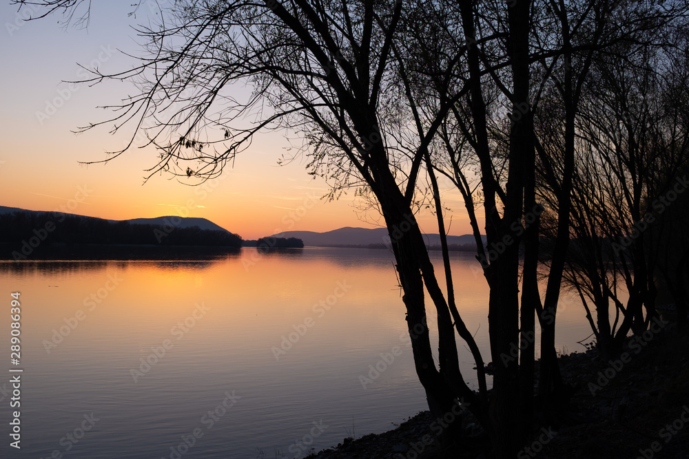 River coast with trees and mountain silhouettes at sunset (Danube river, Hungary)