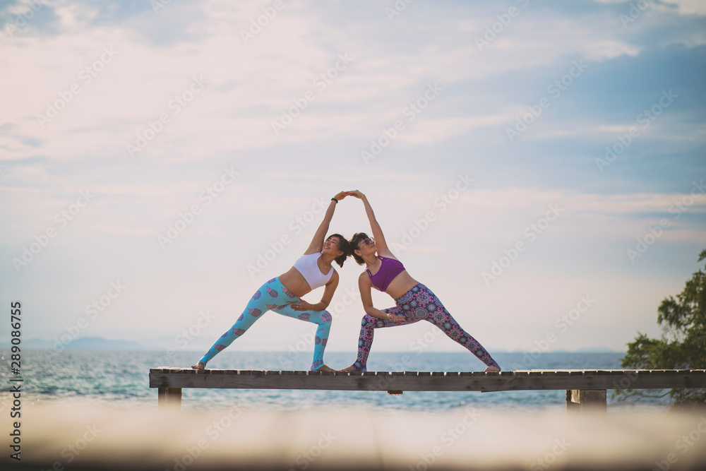 couples of woman playing yoga pose on beach pier with moring sun light