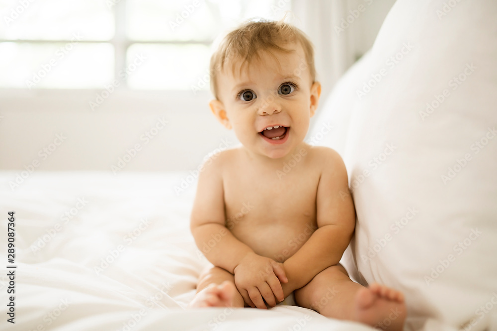 Cute happy baby girl in diaper on bed