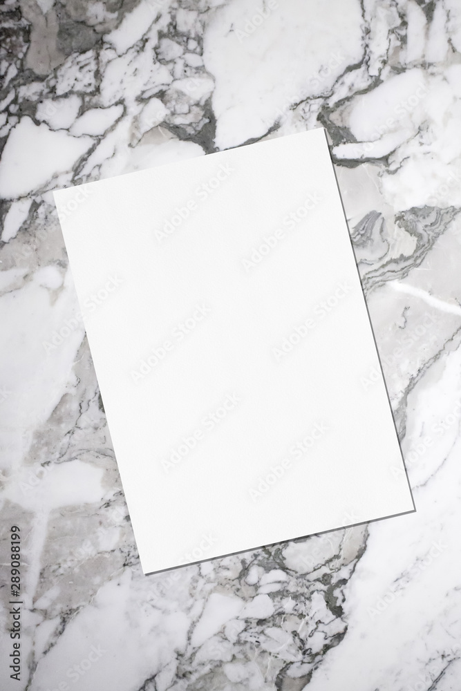 Empty white vertical rectangle poster or business card mockup with soft shadow lying diagonally on grey marble background. Flat lay, top view Empty white vertical rectangle poster or business card mockup with soft shadow lying diagonally on grey marble background. Flat lay, top view