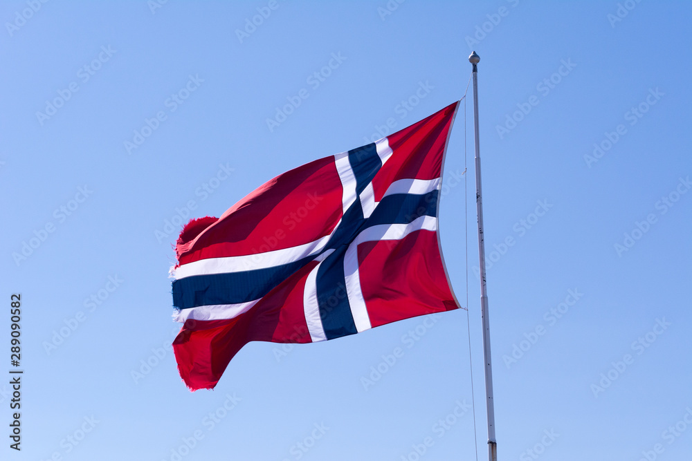 Flag of Norway waving in the wind, on a pole, against blue sky. 