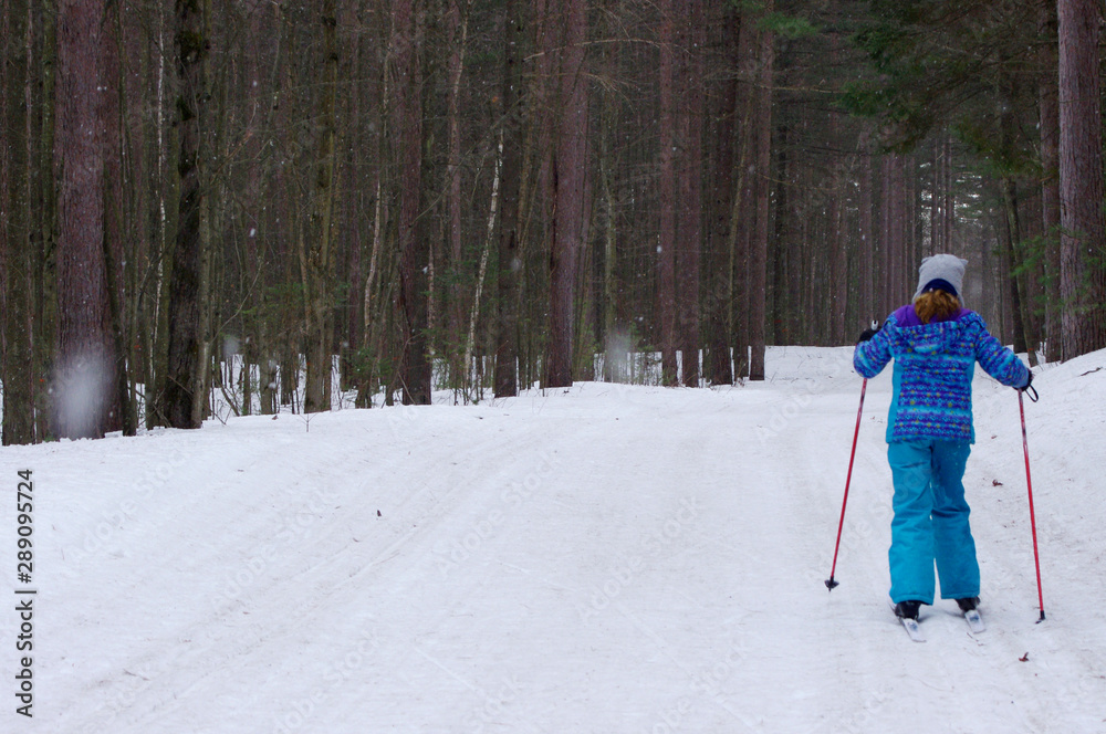 Girl cross-country skiing in woods while it snows
