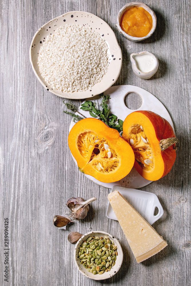 Ingredients for cooking pumpkin risotto. Raw uncooked risotto rice in ceramic bowl, sliced pumpkin, cream, seeds, parmesan cheese, garlic and herbs over grey wooden background. Flat lay, space Ingredients for cooking pumpkin risotto. Raw uncooked risotto rice in ceramic bowl, sliced pumpkin, cream, seeds, parmesan cheese, garlic and herbs over grey wooden background. Flat lay, space