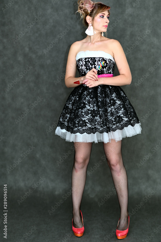 Full-length vertical portrait of a cute happy funny blonde girl with colored hair in a cheerful dress on a gray background with candy in her hands. Smiling in various poses, beauty, holiday. Full-length vertical portrait of a cute happy funny blonde girl with colored hair in a cheerful dress on a gray background with candy in her hands. Smiling in various poses, beauty, holiday.