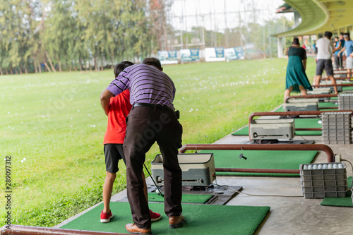 Personal trainer giving lesson to young boy in golf driving range.