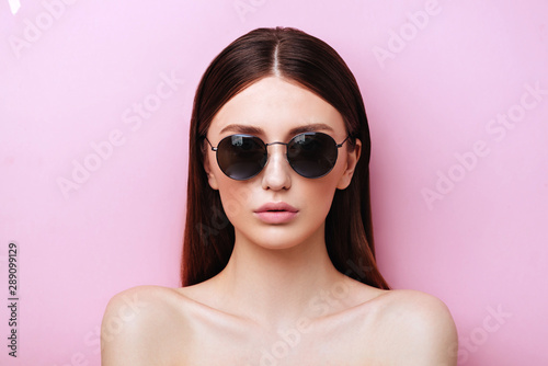Portrait of an attractive young girl in round glasses on a pink background in studio © Margo Basarab