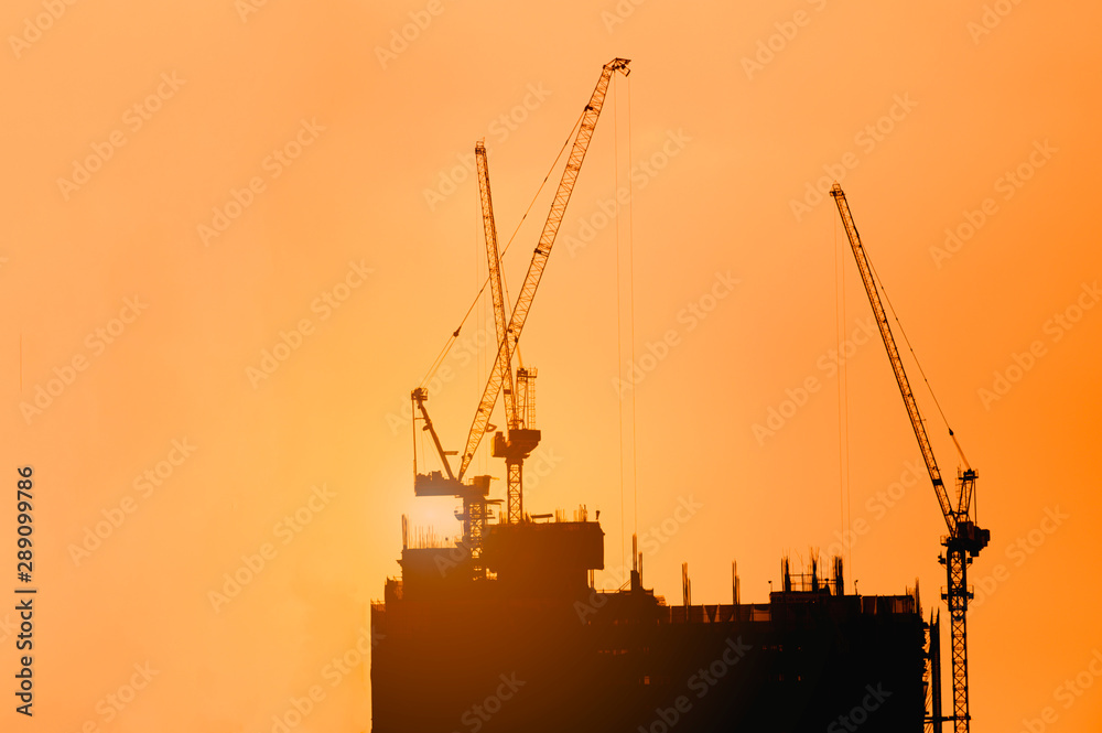 Silhouette of building construction site including several cranes working on a building complex, with sunset.