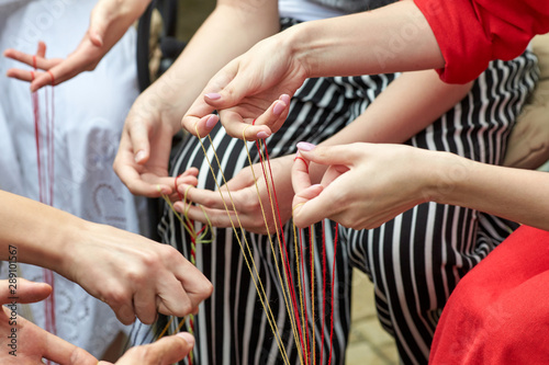 Closeup of female hands weaving shoelaces from colored threads.