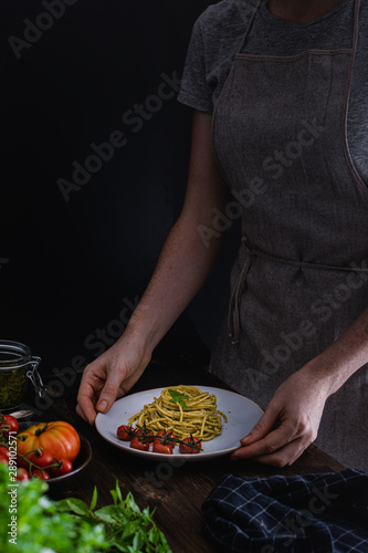 Spaghetti pasta with basil pesto and tomatoes, wooden table