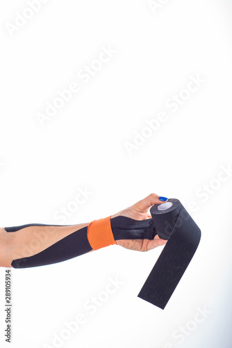 Physiotherapy for a diseased wrist. Alternative medicine. Adhesive tape for athletes with injuries. Support for an injured arm. Female hand on a white background holds a roll of kinesiotape.