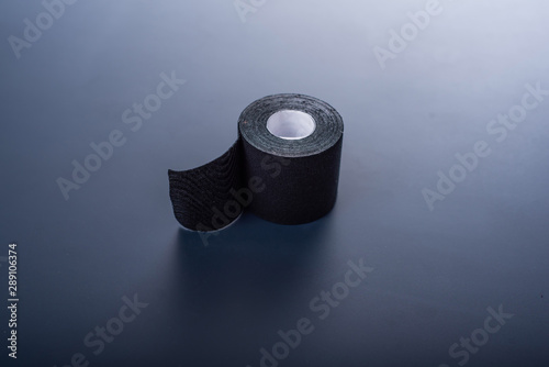 The medical tape lies on a black background. Black roll of kineziotape. Sports patch, designed to maintain muscles, joints and outflow of lymph. photo