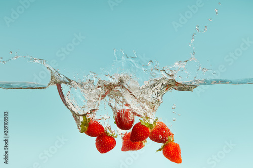 ripe strawberries falling in water with splash on blue background
