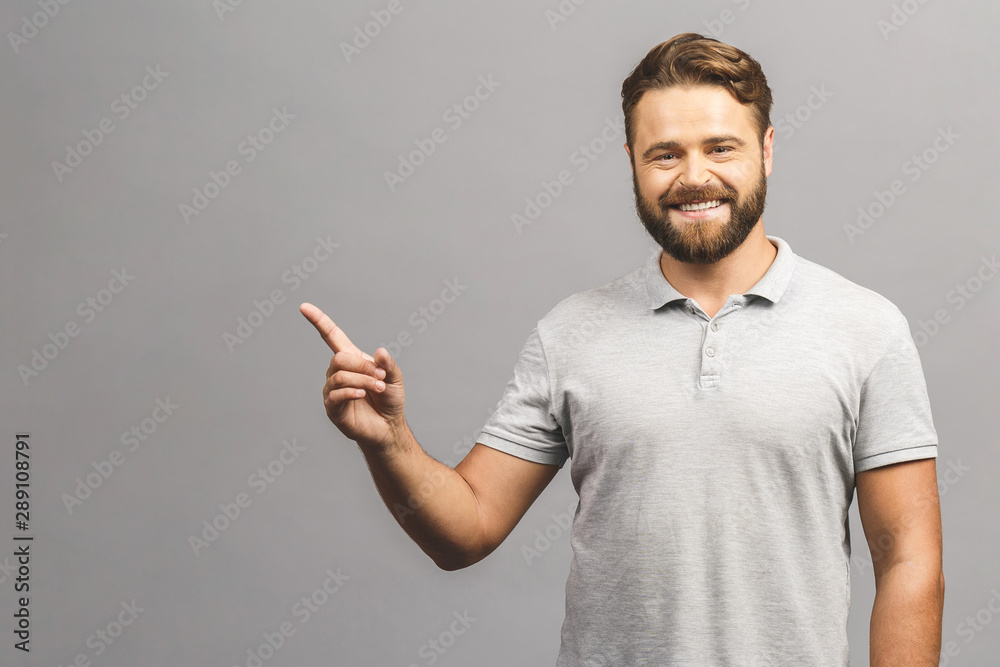 Look over there! Happy young handsome man in jeans shirt pointing away and smiling while standing against white background Look over there! Happy young handsome man in jeans shirt pointing away and smiling while standing against white background