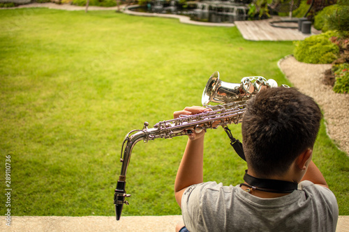 Rearview of Asian young boy holding saxophone in hands at courtyard
