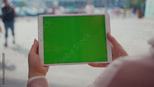 Young hands woman using tablet device computer with green screen outdoors in street at sunlight horizontal bloom message pad technology chroma key female digital girl app chat finger slow motion