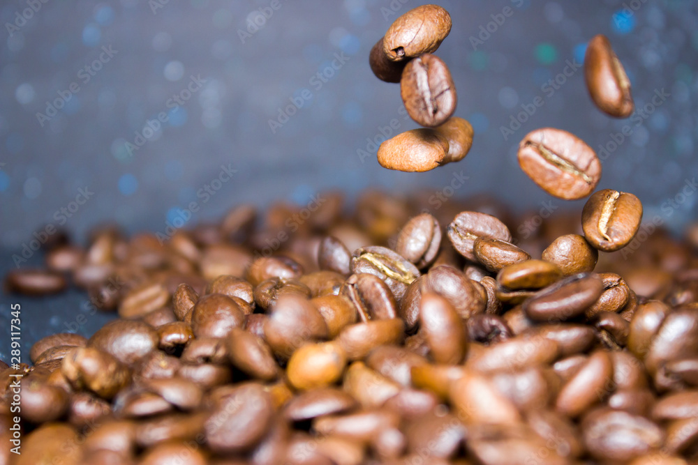 Obraz premium Roasted coffee beans pour from above, hovering in the air on a dark background. Side view, close-up