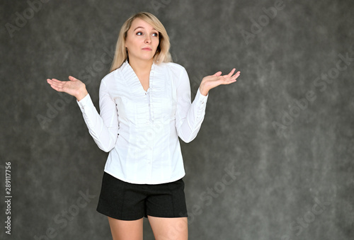 Portrait of a pretty blonde manager girl in a white blouse on a gray background. Right in front of the camera in various poses.