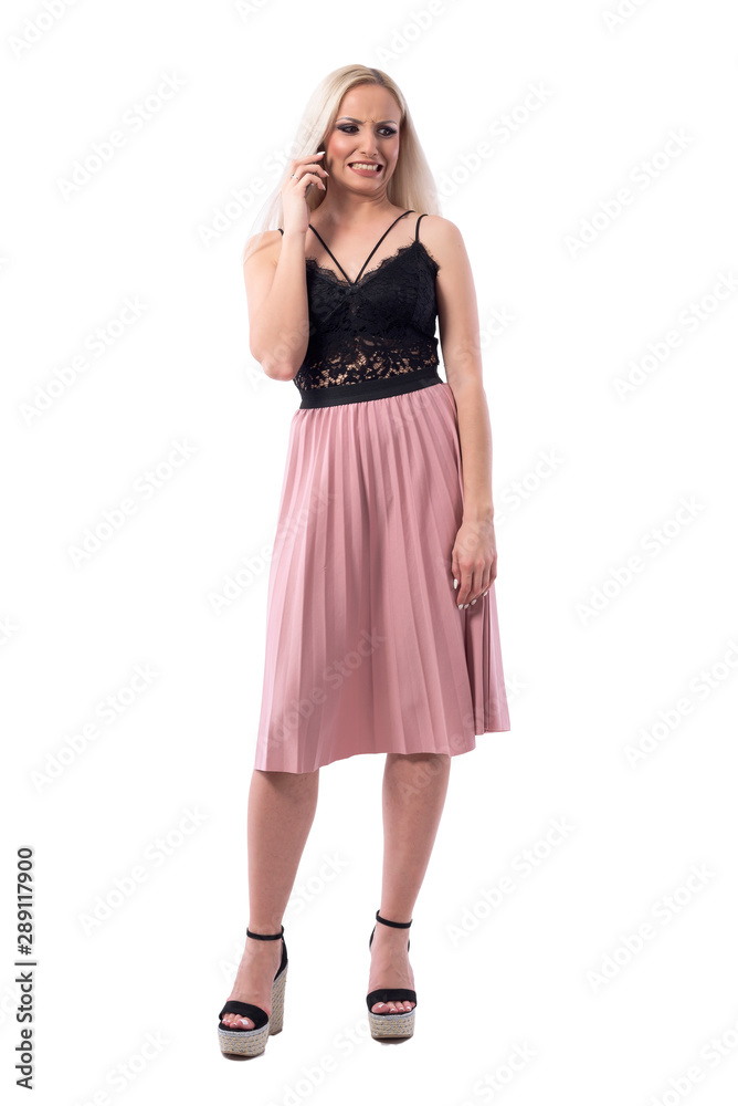 Young blonde woman talking on the phone with disgusted face expression. Full body isolated on white background.