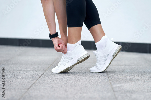 Closeup of female legs in black sport leggings in stylish white sneakers. Active slim woman on a training. Ready to start.