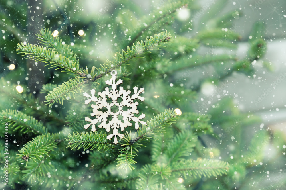Wooden handmade Christmas tree decorations in shape of snowflake hang on green Christmas tree and snowing. Natural materials in life, holiday background. Wooden handmade Christmas tree decorations in shape of snowflake hang on green Christmas tree and snowing. Natural materials in life, holiday background.