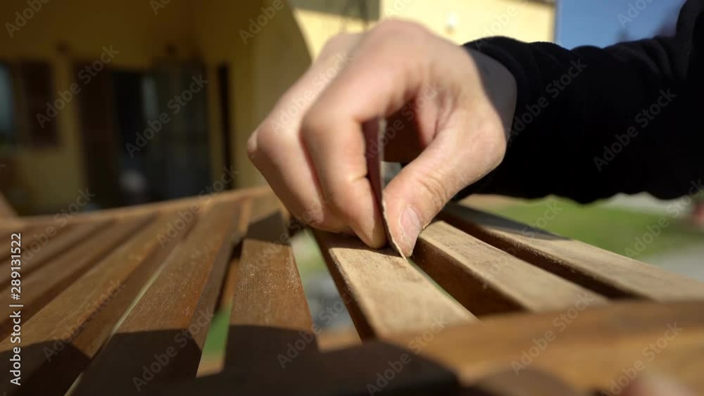Closeup of carpenter's hand restoring a wooden chair with sandpaper. Garden furniture. Macro shot. Closeup of carpenter's hand restoring a wooden chair with sandpaper. Garden furniture. Macro shot.