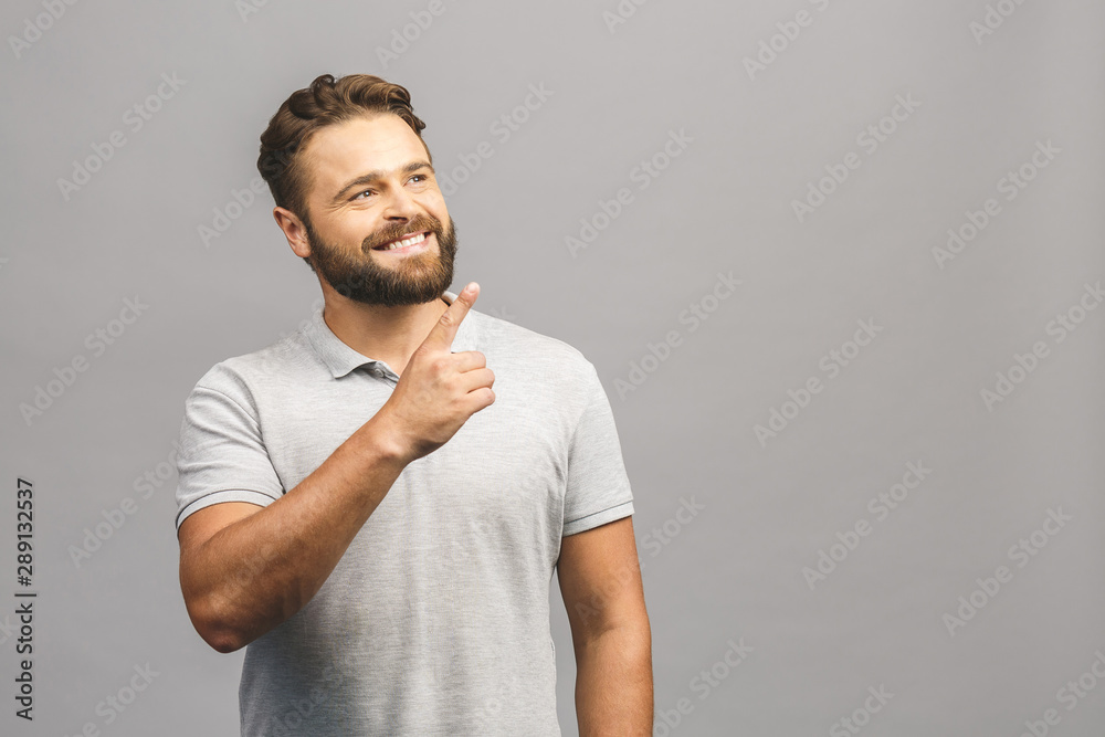 Look over there! Happy young handsome man in casual pointing away and smiling while standing against grey background Look over there! Happy young handsome man in casual pointing away and smiling while standing against grey background