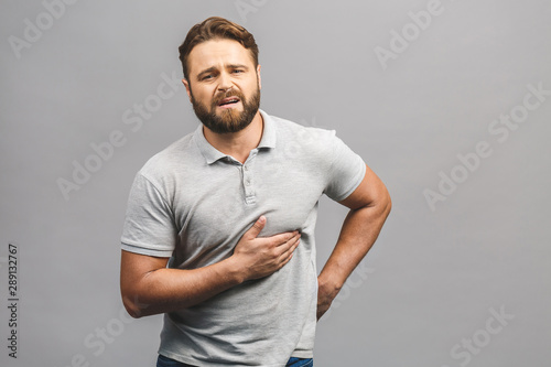 Broken heart concept. Portrait of grimacing sad upset nervous unhappy frustrated exhausted bearded man placing hands on chest suffering from pain in heart isolated on gray background copy-space