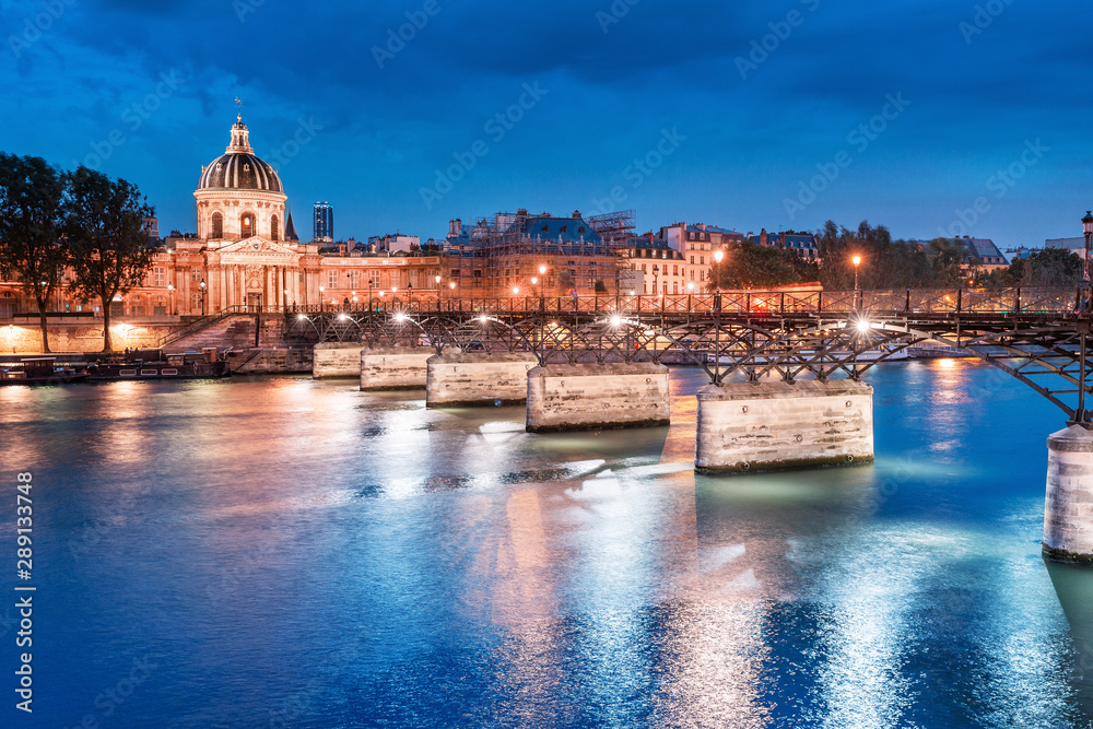 Night cityscape with illuminated academic building Institut de France and pedestrian bridge with lanterns over the river Seine in Paris, France