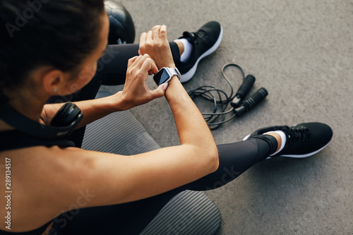 High angle view of female using smart watch. Unrecognizable woman sitting on mat outdoors checking activity wrist tracker. photo