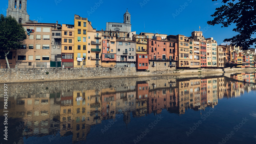 Girona city skyline with river houses colourful facades reflected on quiet river water on a blue summer sunny sky