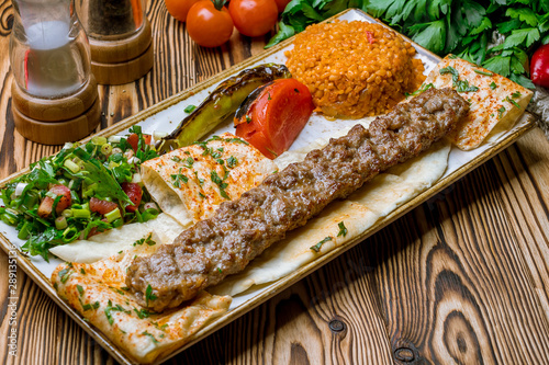 Fotografia lula kebab from lamb in Turkish on the board with bulgur and vegetables