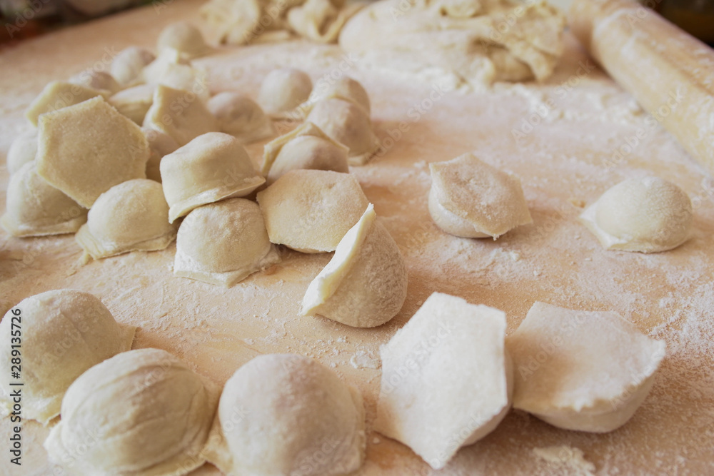 Raw dumplings are scattered on a wooden board sprinkled with flour. Cooking a national dish.