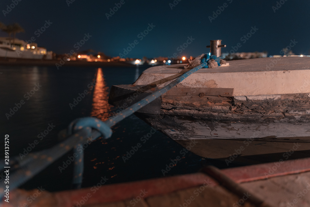 Fototapeta premium long time exposure of a boat in El gouna lagoon with a view of a hotel in the night and stars in the air.