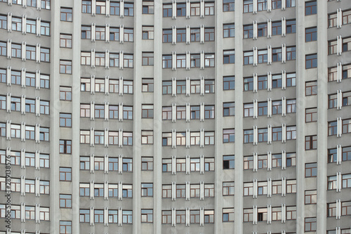 The facade of a tall office building with numerous windows. Architecture of the mid-twentieth century. A monumental building made of reinforced concrete. Wall of an apartment building. Layout design