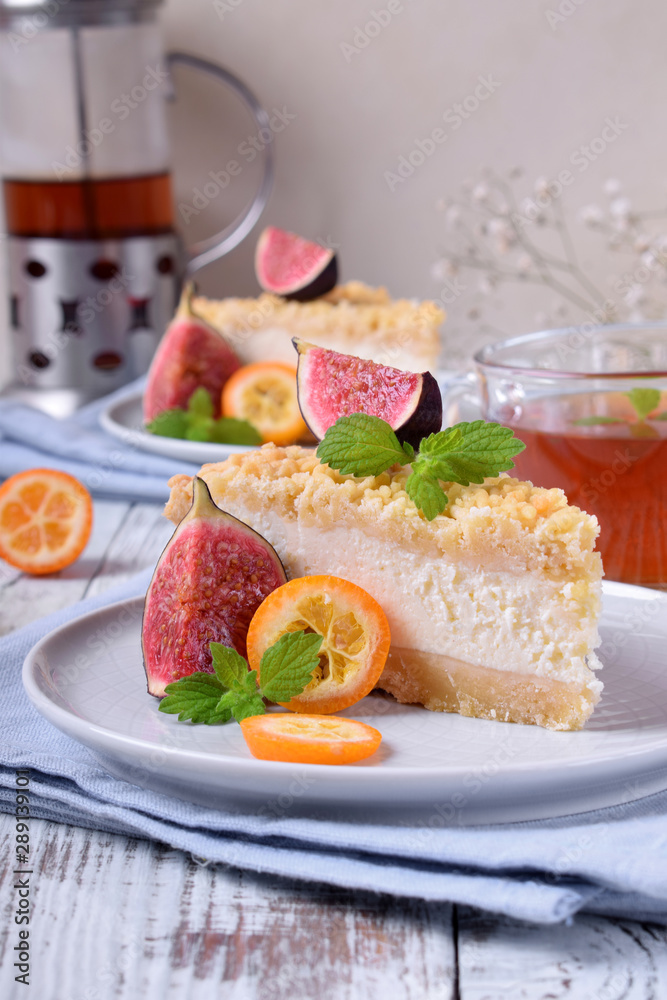 Piece of grated pie with cottage cheese topped with figs and kumquats on ceramic plate on white wooden table