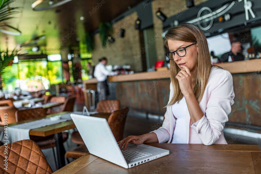 Image of woman using laptop while sitting at her desk. Young businesswoman sitting in the coffee shop and working on laptop. Digital displays surrounding us from everywhere Image of woman using laptop while sitting at her desk. Young businesswoman sitting in the coffee shop and working on laptop. Digital displays surrounding us from everywhere