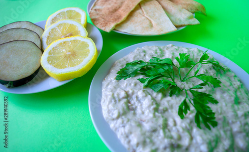 Famous traditional Arabic cuisine - dip Baba ganoush with pita bread and fresh lemon on green background. Flat lay, top view. Baba ganoush. 