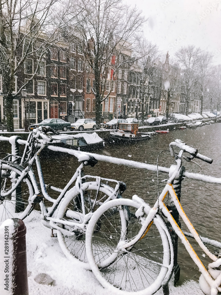 Snowy bicycles on the bridge in the city center Amsterdam Netherlands. Blizzard on winter in the Netherlands. Bicycles covered with snow on a bridge. Snowfall in capital Netherlands