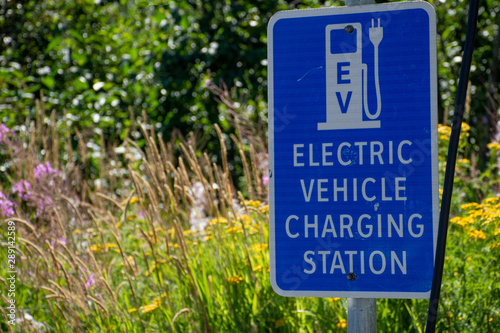 Electric vehicle only charging station sign for environmentally friendly vehicles with a green grass and flower background.