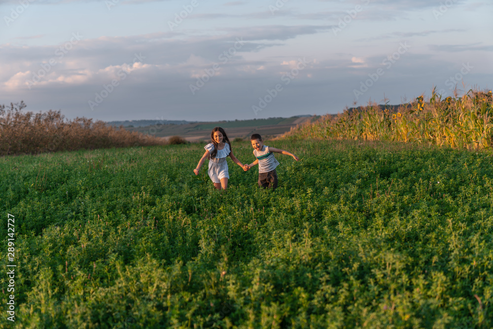 Happy smiling teen boy and girl in casual clothes holding hands together and running across the green field Happy smiling teen boy and girl in casual clothes holding hands together and running across the green field