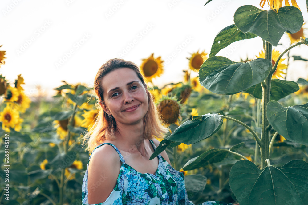 Close up portrait of the beautiful young woman with natural healthy skin that smiling and looking at the camera, standing among sunflowers Close up portrait of the beautiful young woman with natural healthy skin that smiling and looking at the camera, standing among sunflowers
